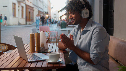 Arabian Indian man ethnic guy customer tourist businessman male freelancer video call laptop conference internet chatting talking in headphones friendly online meeting in city cafe outdoors smiling