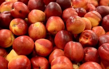 A lot of fresh red yellow colored peaches on market stall or in groceries shop area. Nectarines background. Fruit food background. Close-up