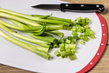 A bunch of green onion on a cutting board with a knife and some cut up onion