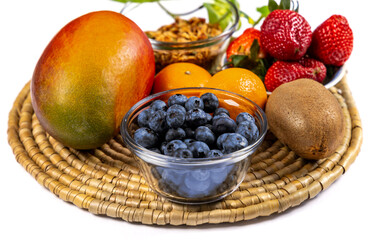 mango, kiwi, strawberry, oranges, and blueberry fruit for salad on a woven place mat isolated on white