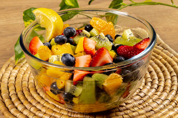 A glass dish of mango kiwi strawberry and blueberry fruit salad on a woven place mat
