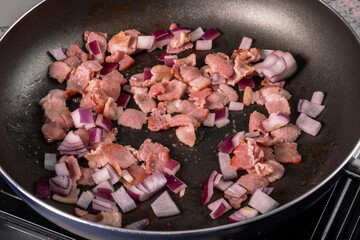 Cut up bacon and red onion frying in a black frying pan