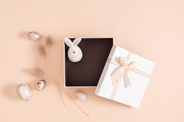 Easter composition with gift and bunny. Minimal Easter background with bunny in gift box on pastel beige background and Easter decorations. Top view.