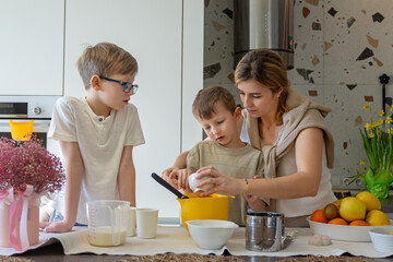 Mother teaching children to bake in kitchen. A mother helps her young son mix ingredients while his...