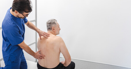 Osteopath examines spine of senior male patient who is sitting. Manual therapist check-up