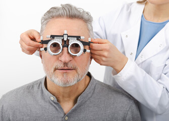 Senior man wearing optometrist trial frame at ophthalmology clinic. Selection of diopter glasses...