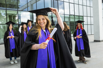 Portrait of graduate student standing in front of her friends with toga and diploma all happy.