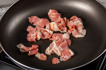 Bacon cut into pieces sizzling in a black frying pan
