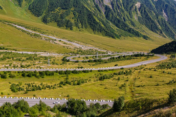 Scenic view of a winding mountain road traversing a vibrant green valley, showcasing the beauty of nature and transportation infrastructure