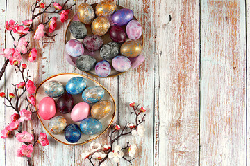 Easter celebration concept, marble Easter eggs painted with hibiscus tea and golden turmeric on a wooden background with sakura branches, ideas for homemade Easter cooking