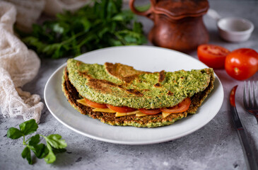 Large oatmeal pancake with spinach, tomatoes and cheese for breakfast on a white plate on a wooden table. Close-up