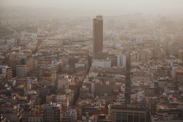 Fototapeta premium Aerial view of a dense urban landscape in Alicante, Spain, with a tall skyscraper standing among low-rise buildings under a hazy sky