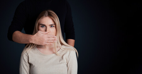 A woman sits quietly with a look of distress as a man covers her mouth. This symbolizes the issues of domestic abuse within millennial relationships, highlighting a grave crisis, copy space