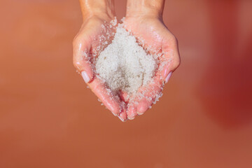 A close-up of a womans hands delicately holding sparkling salt crystals from a pink salt lake, with sunlight reflecting off the crystals and creating a serene, calming atmosphere.