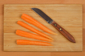 A knife and quartered carrots lie on a wooden cutting board