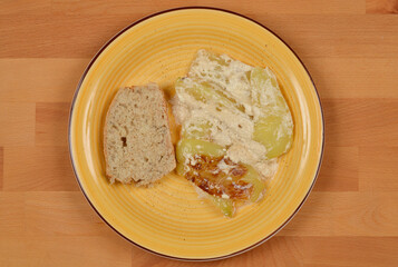 A top-down shot of roasted peppers with sour cream served on a yellow plate alongside a slice of bread, set against a wooden background