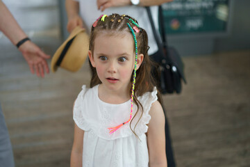 A little girl with small multicolored braids and wide-open eyes in a summer park. Concept of...