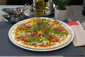 Delicious pizza topped with colorful vegetables savory meat and fresh arugula presented on a restaurant table setting
