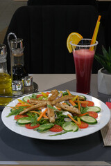 Healthy salad with grilled chicken strips and fresh vegetables served with a vibrant red smoothie with an orange slice on top
