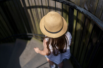 A little girl in a straw hat is descending a spiral staircase in a park. Top-down view. Concept of...
