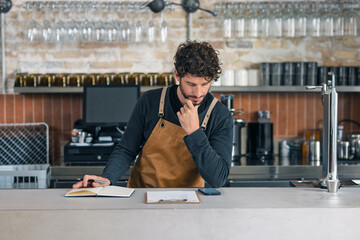 Handsome waiter taking inventory of everything missing while making a checklist on his phone at the...