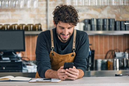 Handsome waiter taking a breakvwhile using smartphone at coffee shop