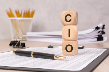 Wooden blocks with the letters "CIO" on a desk with documents, a pen, and office supplies