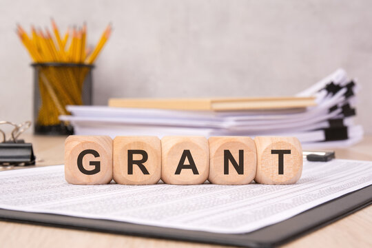 Wooden blocks spelling "GRANT" on a document with office supplies in the background