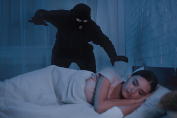 Crime Concept. Masked stalker ready to attack woman who is sleeping in bed at home in the middle of...