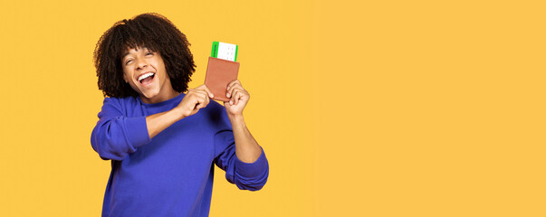 Joyful young man holding passport and boarding passes, happy cheerful african american guy excited...