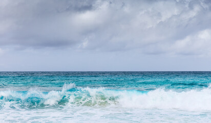 Vivid ocean waves crash under a cloudy sky. Seychelles