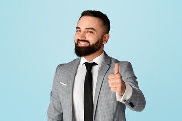 Cheerful millennial businessman showing thumb up gesture against blue background