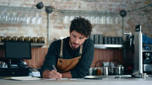 Video of handsome waiter taking a break while using smartphone at coffee shop