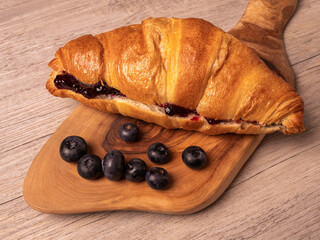 Close-up of jam-filled croissant and fresh blueberries on cutting board. Top view.

