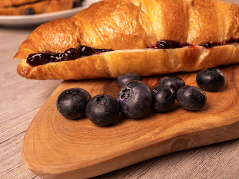 Close-up of jam-filled croissant and fresh blueberries on cutting board
