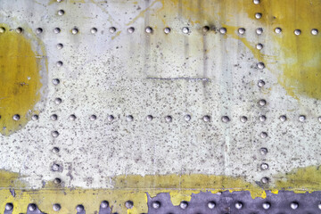 An old riveted with button-head rivets metal plate once painted in yellow and white as a steampunk industrial background