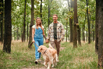 A Joyful Couple Enjoying a Leisurely Walk with Their Beloved Dog in a Lush Green Forest