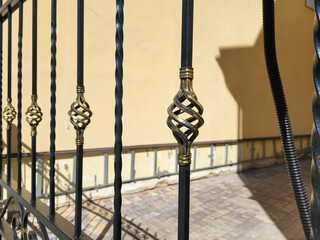 A fence with forged bronze elements on the background of a beige wall of the house