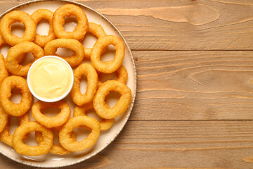 Plate with fried breaded onion rings and mayonnaise on wooden background