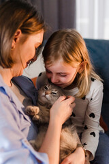 Caucasian family in casual clothes spending time together at home. Mother, son and daughter playing with cat in living room. Brother and sister having fun with mother cuddling with pet at weekend.