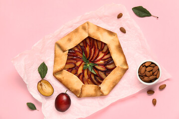 Baking paper with delicious plum galette and bowl of almond on pink background