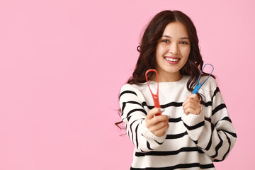 Happy young Asian woman with tongue scrapers on pink background © Pixel-Shot
