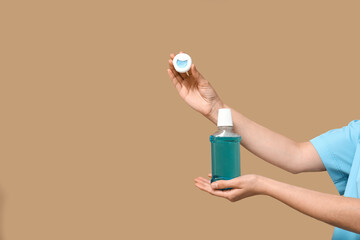 Female hands with dental floss and mouth rinse on beige background