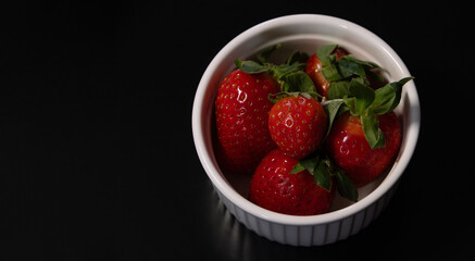 Berries of ripe strawberries in a small bowl on a black background, copy space