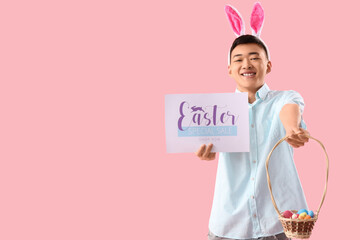 Young Asian man in bunny ears holding paper with text EASTER SPECIAL SALE and basket on pink background