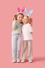 Cute little girls in bunny ears with chocolate Easter eggs hugging on pink background