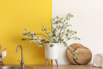 Vase with blooming branches near sink in yellow kitchen