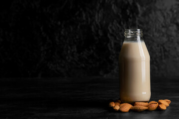 Bottle of fresh almond milk and nuts on black background