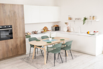 Blurred view of light kitchen with counters, shelf and dining table