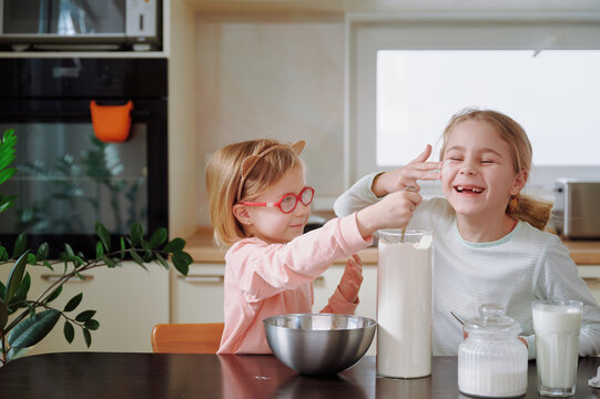 Two girls smear flour on each other’s cheeks, transforming kitchen prep into messy play with giggles and powdery handprints everywhere